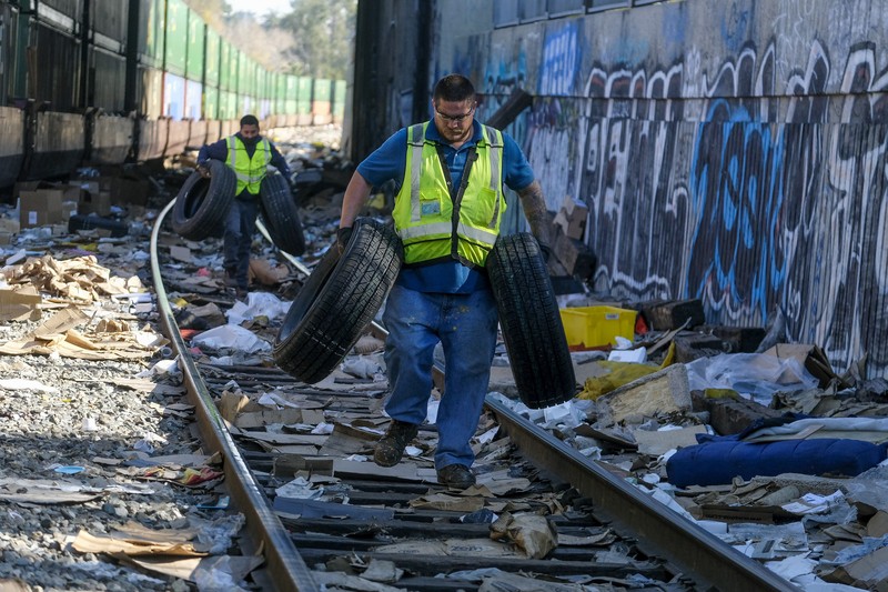 Perampokan Paket di rel kereta as Pekerja kontraktor Adam Rodriguez (depan) dan Luis Rosas mengambil ban kendaraan dari kotak dan paket yang robek di sepanjang bagian rel kereta Union Pacific di pusat kota Los Angeles Jumat (14/1/2022). Pencuri telah merampok kontainer kargo di atas kereta dekat pusat kota Los Angeles selama berbulan-bulan dan juga mereka meninggalkan ratusan kardus dan barang-barang yang menurut para pencuri tidak cukup berharga untuk diambil. (AP/Ringo H.W. Chiu)