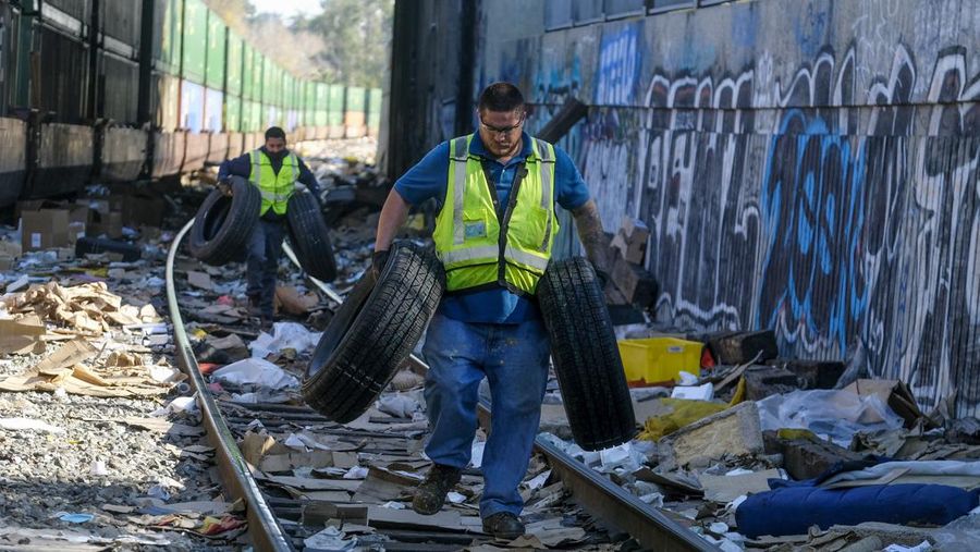Pekerja kontraktor Adam Rodriguez (depan) dan Luis Rosas mengambil ban kendaraan dari kotak dan paket yang robek di sepanjang bagian rel kereta Union Pacific di pusat kota Los Angeles Jumat (14/1/2022).  Pencuri telah merampok kontainer kargo di atas kereta dekat pusat kota Los Angeles selama berbulan-bulan dan juga mereka meninggalkan ratusan kardus dan barang-barang yang menurut para pencuri tidak cukup berharga untuk diambil. (AP/Ringo H.W. Chiu)