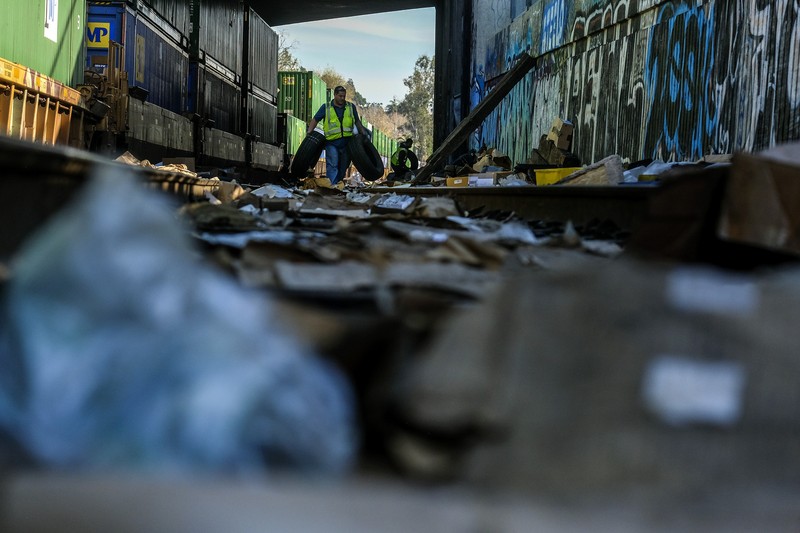 Pekerja kontraktor Adam Rodriguez (depan) dan Luis Rosas mengambil ban kendaraan dari kotak dan paket yang robek di sepanjang bagian rel kereta Union Pacific di pusat kota Los Angeles Jumat (14/1/2022).  Pencuri telah merampok kontainer kargo di atas kereta dekat pusat kota Los Angeles selama berbulan-bulan dan juga mereka meninggalkan ratusan kardus dan barang-barang yang menurut para pencuri tidak cukup berharga untuk diambil. (AP/Ringo H.W. Chiu)