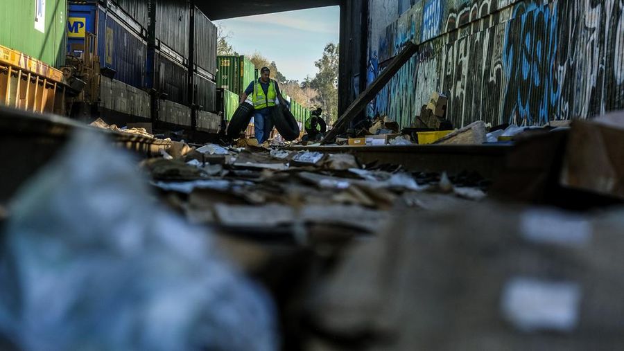 Pekerja kontraktor Adam Rodriguez (depan) dan Luis Rosas mengambil ban kendaraan dari kotak dan paket yang robek di sepanjang bagian rel kereta Union Pacific di pusat kota Los Angeles Jumat (14/1/2022).  Pencuri telah merampok kontainer kargo di atas kereta dekat pusat kota Los Angeles selama berbulan-bulan dan juga mereka meninggalkan ratusan kardus dan barang-barang yang menurut para pencuri tidak cukup berharga untuk diambil. (AP/Ringo H.W. Chiu)
