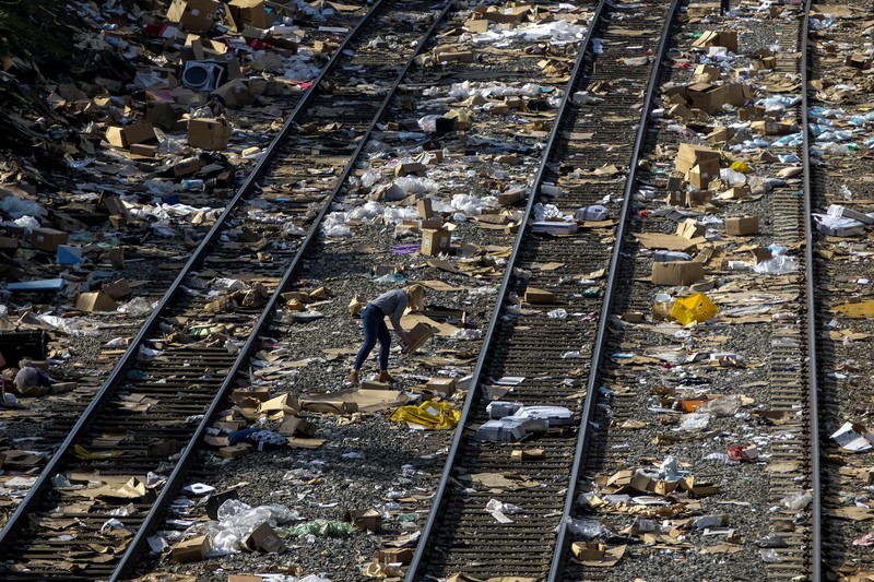 Pekerja kontraktor Adam Rodriguez (depan) dan Luis Rosas mengambil ban kendaraan dari kotak dan paket yang robek di sepanjang bagian rel kereta Union Pacific di pusat kota Los Angeles Jumat (14/1/2022).  Pencuri telah merampok kontainer kargo di atas kereta dekat pusat kota Los Angeles selama berbulan-bulan dan juga mereka meninggalkan ratusan kardus dan barang-barang yang menurut para pencuri tidak cukup berharga untuk diambil. (AP/Ringo H.W. Chiu)