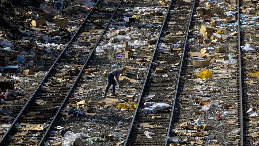 Pekerja kontraktor Adam Rodriguez (depan) dan Luis Rosas mengambil ban kendaraan dari kotak dan paket yang robek di sepanjang bagian rel kereta Union Pacific di pusat kota Los Angeles Jumat (14/1/2022).  Pencuri telah merampok kontainer kargo di atas kereta dekat pusat kota Los Angeles selama berbulan-bulan dan juga mereka meninggalkan ratusan kardus dan barang-barang yang menurut para pencuri tidak cukup berharga untuk diambil. (AP/Ringo H.W. Chiu)