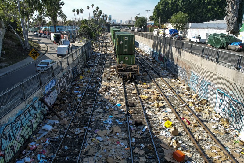 Perampokan Paket di rel kereta as Pekerja kontraktor Adam Rodriguez (depan) dan Luis Rosas mengambil ban kendaraan dari kotak dan paket yang robek di sepanjang bagian rel kereta Union Pacific di pusat kota Los Angeles Jumat (14/1/2022). Pencuri telah merampok kontainer kargo di atas kereta dekat pusat kota Los Angeles selama berbulan-bulan dan juga mereka meninggalkan ratusan kardus dan barang-barang yang menurut para pencuri tidak cukup berharga untuk diambil. (AP/Ringo H.W. Chiu)