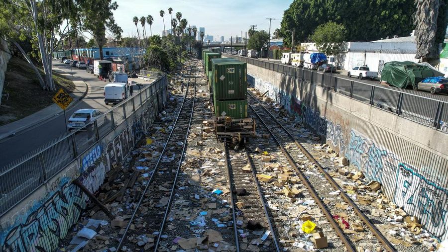 Pekerja kontraktor Adam Rodriguez (depan) dan Luis Rosas mengambil ban kendaraan dari kotak dan paket yang robek di sepanjang bagian rel kereta Union Pacific di pusat kota Los Angeles Jumat (14/1/2022).  Pencuri telah merampok kontainer kargo di atas kereta dekat pusat kota Los Angeles selama berbulan-bulan dan juga mereka meninggalkan ratusan kardus dan barang-barang yang menurut para pencuri tidak cukup berharga untuk diambil. (AP/Ringo H.W. Chiu)