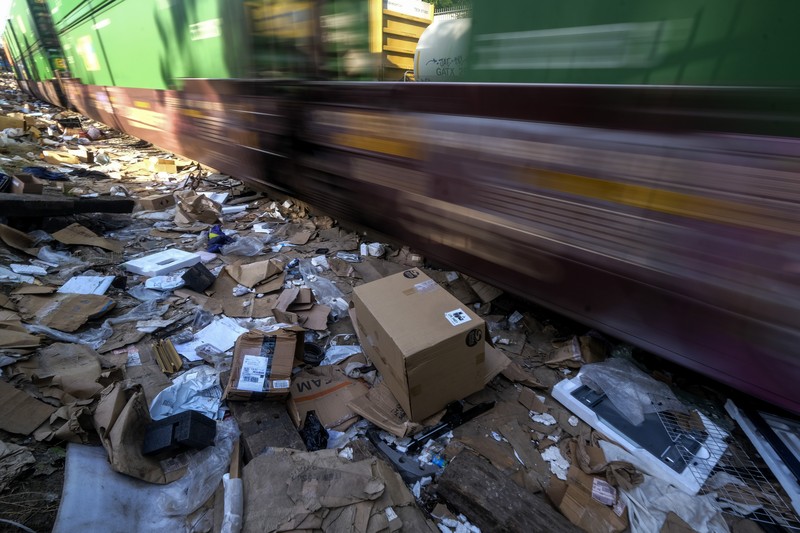 Perampokan Paket di rel kereta as Pekerja kontraktor Adam Rodriguez (depan) dan Luis Rosas mengambil ban kendaraan dari kotak dan paket yang robek di sepanjang bagian rel kereta Union Pacific di pusat kota Los Angeles Jumat (14/1/2022). Pencuri telah merampok kontainer kargo di atas kereta dekat pusat kota Los Angeles selama berbulan-bulan dan juga mereka meninggalkan ratusan kardus dan barang-barang yang menurut para pencuri tidak cukup berharga untuk diambil. (AP/Ringo H.W. Chiu)