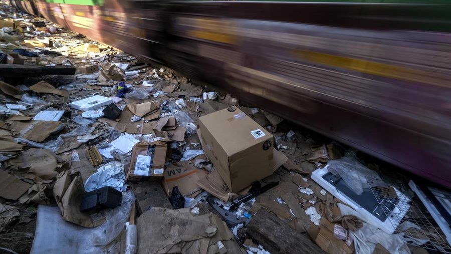 Pekerja kontraktor Adam Rodriguez (depan) dan Luis Rosas mengambil ban kendaraan dari kotak dan paket yang robek di sepanjang bagian rel kereta Union Pacific di pusat kota Los Angeles Jumat (14/1/2022).  Pencuri telah merampok kontainer kargo di atas kereta dekat pusat kota Los Angeles selama berbulan-bulan dan juga mereka meninggalkan ratusan kardus dan barang-barang yang menurut para pencuri tidak cukup berharga untuk diambil. (AP/Ringo H.W. Chiu)
