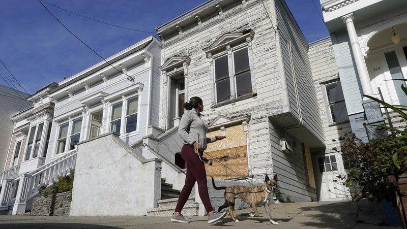 A pedestrian walks a dog past a recently sold Victorian home in San Francisco, Friday, Jan. 14, 2022. The decaying, 122-year-old Victorian marketed as 