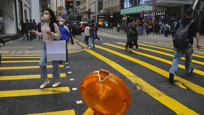 People wearing face masks walk across a street in Hong Kong, Tuesday, Jan. 18, 2022. Hong Kong police arrested two former flight attendants for allegedly leaving their homes when they should have been in isolation for possible coronavirus infections, which were later confirmed. (AP Photo/Kin Cheung)