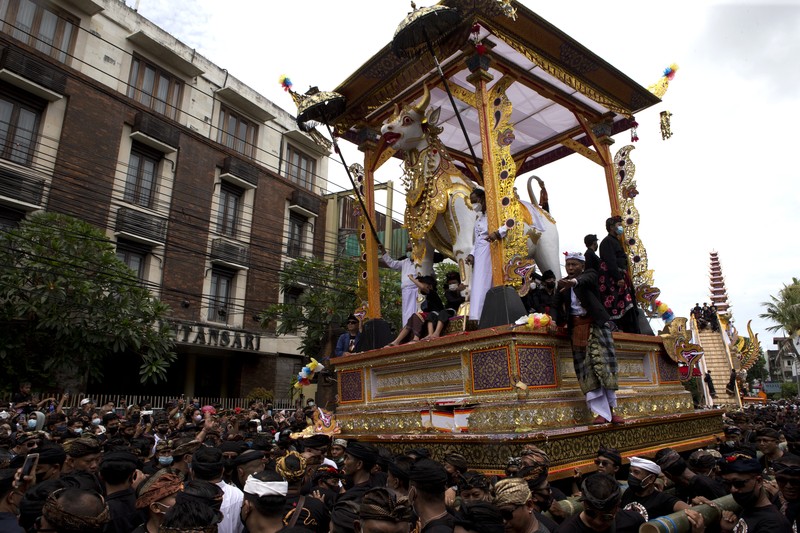 A crowd of people watch a giant sarcophagus in the form of a bull during a procession of King Ida Cokorda Pemecutan XI in Denpasar, Bali, Indonesia on Friday, Jan. 21, 2022. (AP Photo/Firdia Lisnawati)