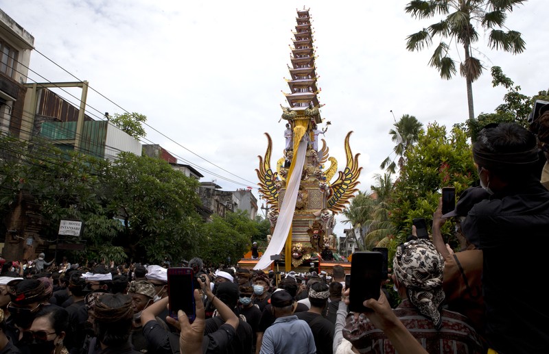 A crowd of people watch a giant sarcophagus in the form of a bull during a procession of King Ida Cokorda Pemecutan XI in Denpasar, Bali, Indonesia on Friday, Jan. 21, 2022. (AP Photo/Firdia Lisnawati)