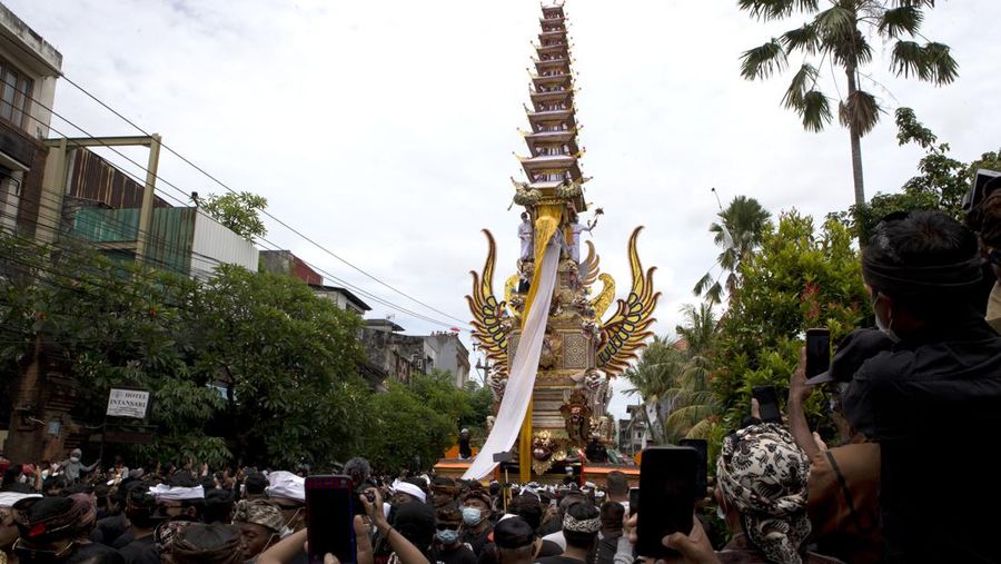 A crowd of people watch men carry an eleven-story cremation tower which contains the body of King Ida Cokorda Pemecutan XI during a cremation ceremony in Denpasar, Bali, Indonesia on Friday, Jan. 21, 2022. (AP Photo/Firdia Lisnawati)