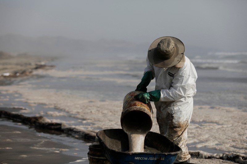 Otoritas setempat dan pekerja kilang La Pampilla, Peru, membersihkan tumpahan minyak di lepas pantai Ventanilla. Tumpahan minyak ini terjadi akibat gelombang tsunami yang dipicu letusan gunung api bawah laut di Tonga. (REUTERS/PILAR OLIVARES)