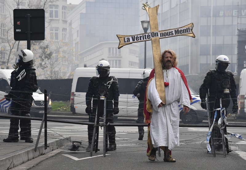 Demo Tolak Vaksin di Brussels Belgia Seorang pengunjuk rasa berbaris dengan salib di dekat markas besar Uni Eropa selama demonstrasi menentang vaksin COVID-19 di Brussels, Minggu (23/1/2022). Demonstran berkumpul di ibukota Belgia untuk memprotes apa yang mereka anggap sebagai tindakan yang terlalu ekstrem oleh pemerintah untuk memerangi COVID -19 pandemi, termasuk izin vaksin yang mengatur akses ke tempat dan kegiatan tertentu dan kemungkinan vaksin wajib. Cross berbunyi 'Kebenaran yang membuat kita dibohongi'. (AP Photo/Geert Vanden Wijngaert)