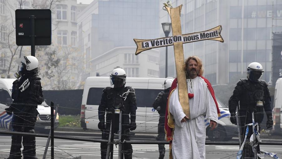 Seorang pengunjuk rasa berbaris dengan salib di dekat markas besar Uni Eropa selama demonstrasi menentang vaksin COVID-19 di Brussels, Minggu (23/1/2022). Demonstran berkumpul di ibukota Belgia untuk memprotes apa yang mereka anggap sebagai tindakan yang terlalu ekstrem oleh pemerintah untuk memerangi COVID -19 pandemi, termasuk izin vaksin yang mengatur akses ke tempat dan kegiatan tertentu dan kemungkinan vaksin wajib. Cross berbunyi 'Kebenaran yang membuat kita dibohongi'. (AP Photo/Geert Vanden Wijngaert)