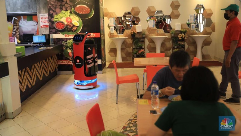 Bellabot, robot pesan-antar makanan sedang diujicoba di area Food Temptation Mal Kelapa Gading Jakarta, Senin (24/1/2022). Penggunaan robot ditujukan mempermudah mitra driver saat menggunakan fitur order sekaligus sehingga cukup mengambil pesanan di satu titik pengumpulan (pick up point) dan mengurangi antrean. Layanan pesan antar makanan GoFood memperkenalkan teknologi robot otomatis untuk mendukung pemesanan makanan melalui fitur Order Sekaligus. Inovasi ini menempatkan GoFood sebagai perusahaan pertama yang memanfaatkan Sistem Kendaraan Tak Berawak (unmanned vehicle system/UVS) untuk layanan pesan antar makanan di Indonesia. Robot Otomatis yang digunakan ini berfungsi mengonsolidasi pesanan dalam fitur GoFood Order Sekaligus dari berbagai mitra UMKM yang berada di area Food Temptation MKG. Setelah itu, robot akan menyerahkan pesanan ke gerai kasir sebagai titik pengumpulan. Pesanan yang sudah selesai kemudian bisa diambil mitra pengemudi untuk diantar ke alamat para pemesan. Diharapkan hadirnya inovasi ini juga dapat mempermudah mitra pengemudi dalam mengambil pesanan Order Sekaligus. Order Sekaligus sendiri adalah salah satu fitur GoFood yang memungkinkan pelanggan memesan makanan/minuman dari banyak resto sekaligus di satu lokasi melalui satu pengiriman. Fitur Order Sekaligus kini bisa dimanfaatkan di 41 lokasi di 7 kota besar termasuk Jabodetabek, Bandung dan Surabaya. Hingga pertengahan 2021, ekspansi lokasi untuk Order Sekaligus ini meningkat 8 kali sejak diperkenalkan pada September 2020.  (CNBC Indonesia/ Muhammad Sabki)