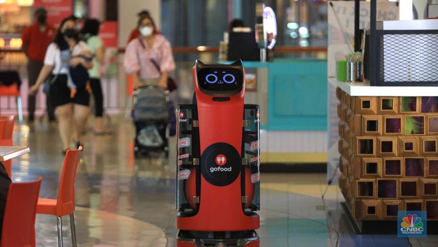 Bellabot, robot pesan-antar makanan sedang diujicoba di area Food Temptation Mal Kelapa Gading Jakarta, Senin (24/1/2022). Penggunaan robot ditujukan mempermudah mitra driver saat menggunakan fitur order sekaligus sehingga cukup mengambil pesanan di satu titik pengumpulan (pick up point) dan mengurangi antrean. Layanan pesan antar makanan GoFood memperkenalkan teknologi robot otomatis untuk mendukung pemesanan makanan melalui fitur Order Sekaligus. Inovasi ini menempatkan GoFood sebagai perusahaan pertama yang memanfaatkan Sistem Kendaraan Tak Berawak (unmanned vehicle system/UVS) untuk layanan pesan antar makanan di Indonesia. Robot Otomatis yang digunakan ini berfungsi mengonsolidasi pesanan dalam fitur GoFood Order Sekaligus dari berbagai mitra UMKM yang berada di area Food Temptation MKG. Setelah itu, robot akan menyerahkan pesanan ke gerai kasir sebagai titik pengumpulan. Pesanan yang sudah selesai kemudian bisa diambil mitra pengemudi untuk diantar ke alamat para pemesan. Diharapkan hadirnya inovasi ini juga dapat mempermudah mitra pengemudi dalam mengambil pesanan Order Sekaligus. Order Sekaligus sendiri adalah salah satu fitur GoFood yang memungkinkan pelanggan memesan makanan/minuman dari banyak resto sekaligus di satu lokasi melalui satu pengiriman. Fitur Order Sekaligus kini bisa dimanfaatkan di 41 lokasi di 7 kota besar termasuk Jabodetabek, Bandung dan Surabaya. Hingga pertengahan 2021, ekspansi lokasi untuk Order Sekaligus ini meningkat 8 kali sejak diperkenalkan pada September 2020.  (CNBC Indonesia/ Muhammad Sabki)