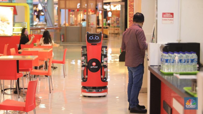 Bellabot, robot pesan-antar makanan sedang diujicoba di area Food Temptation Mal Kelapa Gading Jakarta, Senin (24/1/2022). Penggunaan robot ditujukan mempermudah mitra driver saat menggunakan fitur order sekaligus sehingga cukup mengambil pesanan di satu titik pengumpulan (pick up point) dan mengurangi antrean. Layanan pesan antar makanan GoFood memperkenalkan teknologi robot otomatis untuk mendukung pemesanan makanan melalui fitur Order Sekaligus. Inovasi ini menempatkan GoFood sebagai perusahaan pertama yang memanfaatkan Sistem Kendaraan Tak Berawak (unmanned vehicle system/UVS) untuk layanan pesan antar makanan di Indonesia. Robot Otomatis yang digunakan ini berfungsi mengonsolidasi pesanan dalam fitur GoFood Order Sekaligus dari berbagai mitra UMKM yang berada di area Food Temptation MKG. Setelah itu, robot akan menyerahkan pesanan ke gerai kasir sebagai titik pengumpulan. Pesanan yang sudah selesai kemudian bisa diambil mitra pengemudi untuk diantar ke alamat para pemesan. Diharapkan hadirnya inovasi ini juga dapat mempermudah mitra pengemudi dalam mengambil pesanan Order Sekaligus. Order Sekaligus sendiri adalah salah satu fitur GoFood yang memungkinkan pelanggan memesan makanan/minuman dari banyak resto sekaligus di satu lokasi melalui satu pengiriman. Fitur Order Sekaligus kini bisa dimanfaatkan di 41 lokasi di 7 kota besar termasuk Jabodetabek, Bandung dan Surabaya. Hingga pertengahan 2021, ekspansi lokasi untuk Order Sekaligus ini meningkat 8 kali sejak diperkenalkan pada September 2020.  (CNBC Indonesia/ Muhammad Sabki)