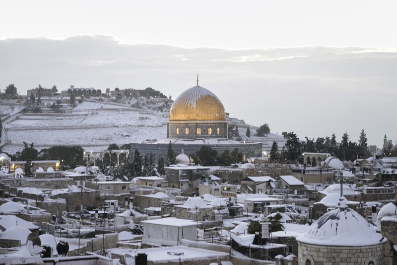 Warga Palestina menikmati salju di sebelah Masjid Kubah Batu di kompleks Masjid Al Aqsa di Kota Tua Yerusalem, Kamis (27/1/2022). Hujan salju yang jarang melanda sebagian wilayah Israel dan Tepi Barat, menutup sekolah dan bisnis. (AP Photo/Mahmoud Illean)