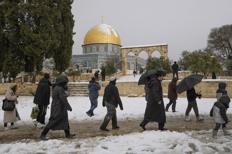 Warga Palestina menikmati salju di sebelah Masjid Kubah Batu di kompleks Masjid Al Aqsa di Kota Tua Yerusalem, Kamis (27/1/2022). Hujan salju yang jarang melanda sebagian wilayah Israel dan Tepi Barat, menutup sekolah dan bisnis. (AP Photo/Mahmoud Illean)