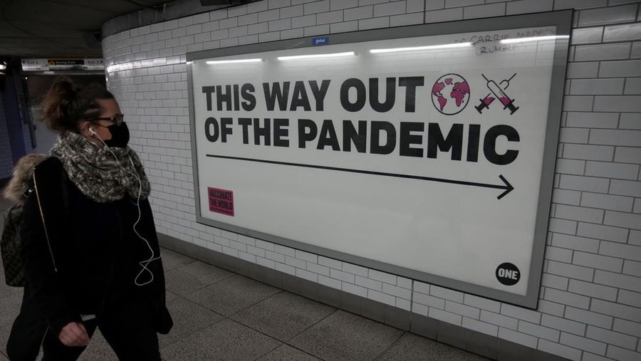 Seorang wanita mengenakan masker untuk mencegah penyebaran virus corona saat berjalan melewati poster kampanye kesehatan dari One NGO di sebuah underpass menuju stasiun kereta bawah tanah Westminster di London, Kamis (27/1/2022).  Sebagian besar pembatasan virus corona termasuk wajib wajah Masker dicabut di Inggris pada hari Kamis, setelah pemerintah Inggris mengatakan peluncuran booster vaksinnya berhasil mengurangi penyakit serius dan rawat inap COVID-19. Mulai Kamis, penutup wajah tidak lagi diwajibkan oleh hukum di mana pun di Inggris. (AP Photo/Matt Dunham)