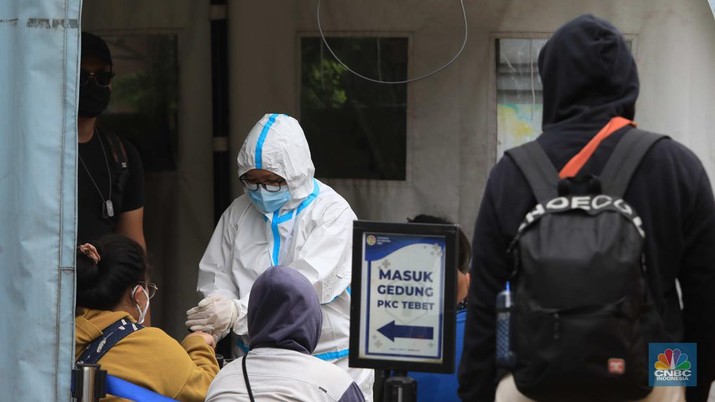 Petugas menggunakan Alat Pelindung Diri (APD) mendata pasien Covid-19 untuk di evakuasi masuk ke dalam bus sekolah di Puskesmas Tebet, Jakarta, Kamis (3/2/2022). (CNBC Indonesia/Muhammad Sabki)