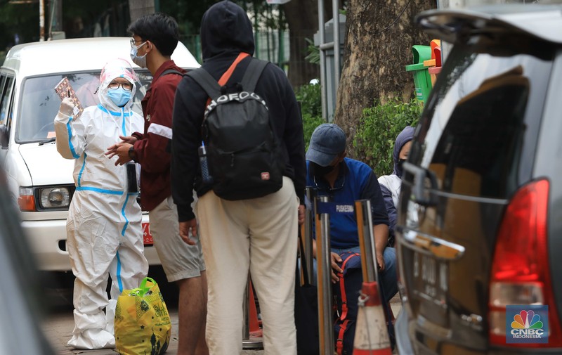 Petugas menggunakan Alat Pelindung Diri (APD) mendata pasien Covid-19 untuk di evakuasi masuk ke dalam bus sekolah di Puskesmas Tebet, Jakarta, Kamis (3/2/2022). (CNBC Indonesia/Muhammad Sabki)