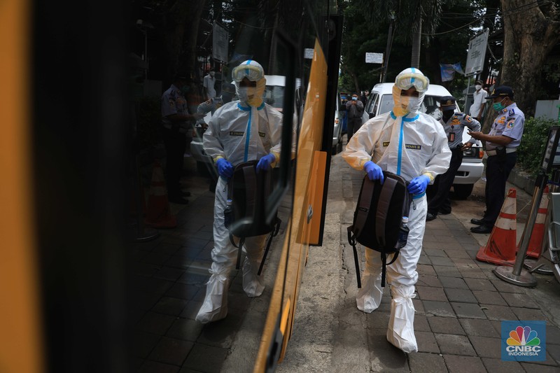 Petugas menggunakan Alat Pelindung Diri (APD) mendata pasien Covid-19 untuk di evakuasi masuk ke dalam bus sekolah di Puskesmas Tebet, Jakarta, Kamis (3/2/2022). (CNBC Indonesia/Muhammad Sabki)