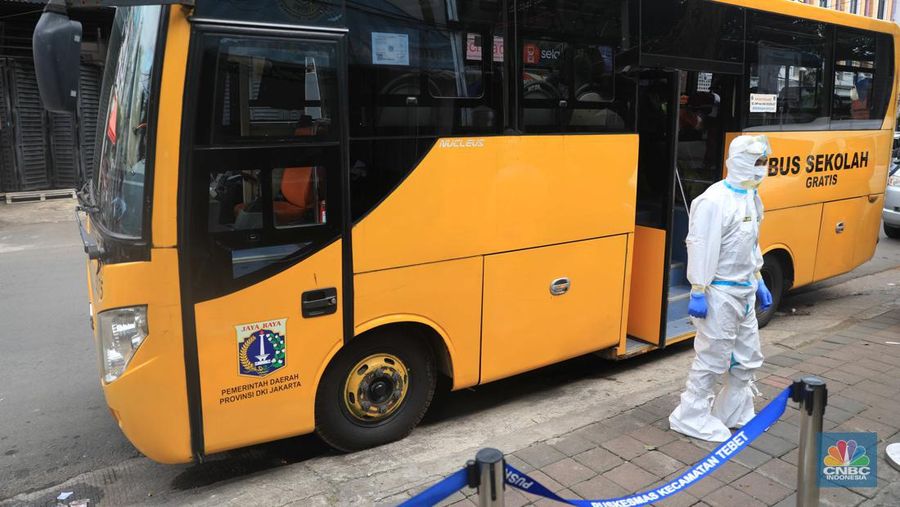 Petugas menggunakan Alat Pelindung Diri (APD) mendata pasien Covid-19 untuk di evakuasi masuk ke dalam bus sekolah di Puskesmas Tebet, Jakarta, Kamis (3/2/2022). (CNBC Indonesia/Muhammad Sabki)