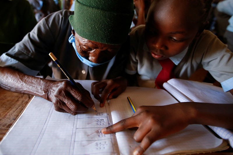 KENYA-EDUCATION/GRANDMA Priscilla Sitienei, a 98-year-old primary school student in grade six, is helped to do an assignment by her classmate at the Leaders Vision Preparatory School in Ndalat village of Nandi County, Kenya January 25, 2022. Picture taken January 25, 2022. REUTERS/Monicah Mwangi