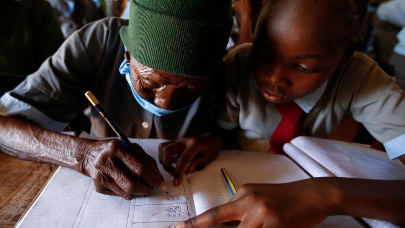 Priscilla Sitienei, a 98-year-old primary school student in grade six, is helped to do an assignment by her classmate at the Leaders Vision Preparatory School in Ndalat village of Nandi County, Kenya January 25, 2022. Picture taken January 25, 2022. REUTERS/Monicah Mwangi
