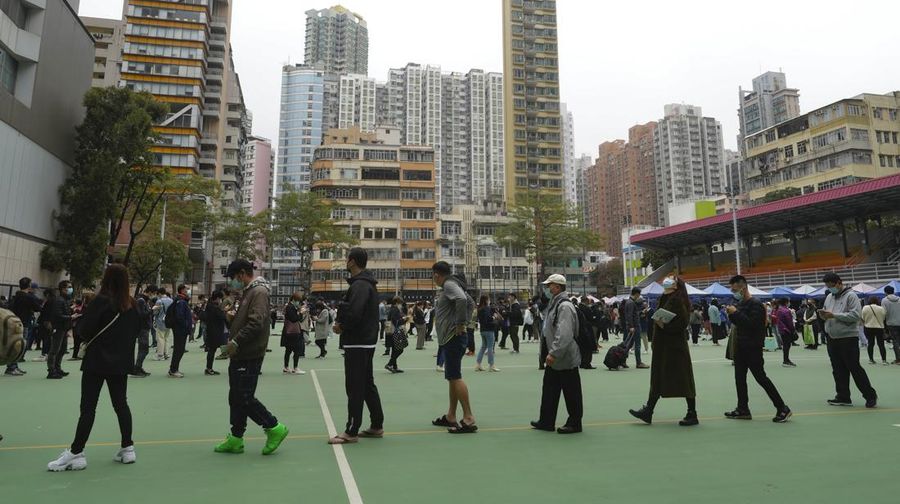 People wearing face masks walk past a huge advertisement banner in Hong Kong, Thursday, Feb. 10, 2022. Hong Kong leader Carrie Lam announced on Tuesday that places of worship and hair salons must close from Thursday until at least Feb. 24, when a “vaccine pass” will be rolled out that permits only vaccinated people to visit venues such as shopping malls and supermarkets. (AP Photo/Vincent Yu)