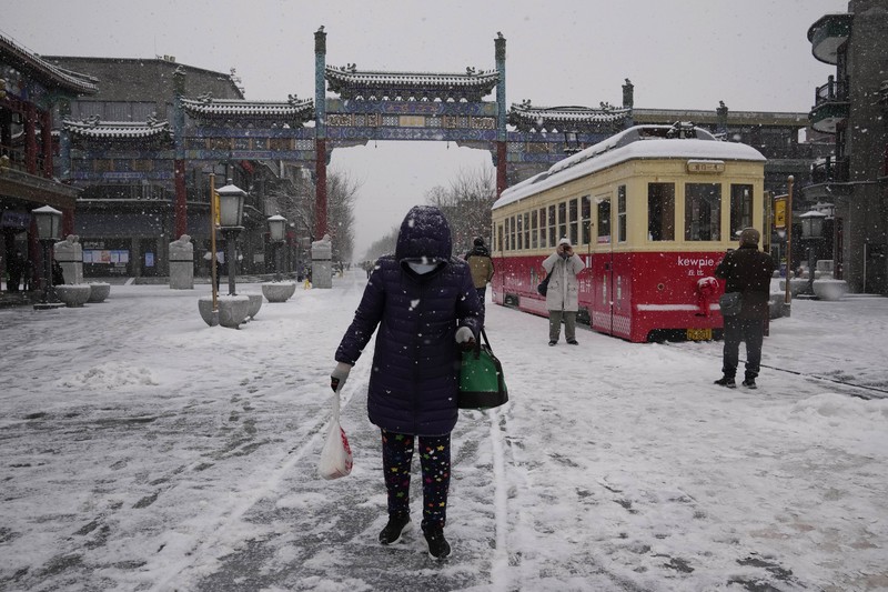 Seorang pria berlari saat salju turun di Beijing, Minggu (13/2/2022). (AP Photo/Mark Baker)