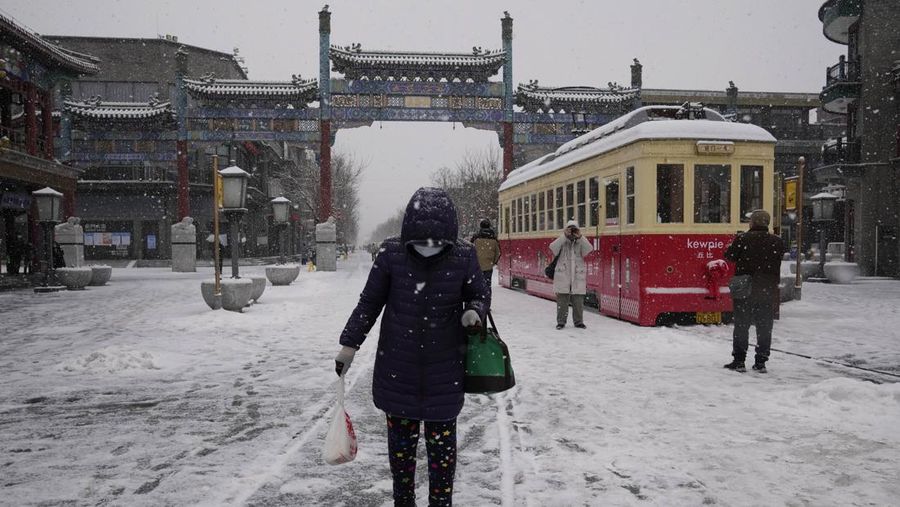 Seorang pria berlari saat salju turun di Beijing, Minggu (13/2/2022). (AP Photo/Mark Baker)