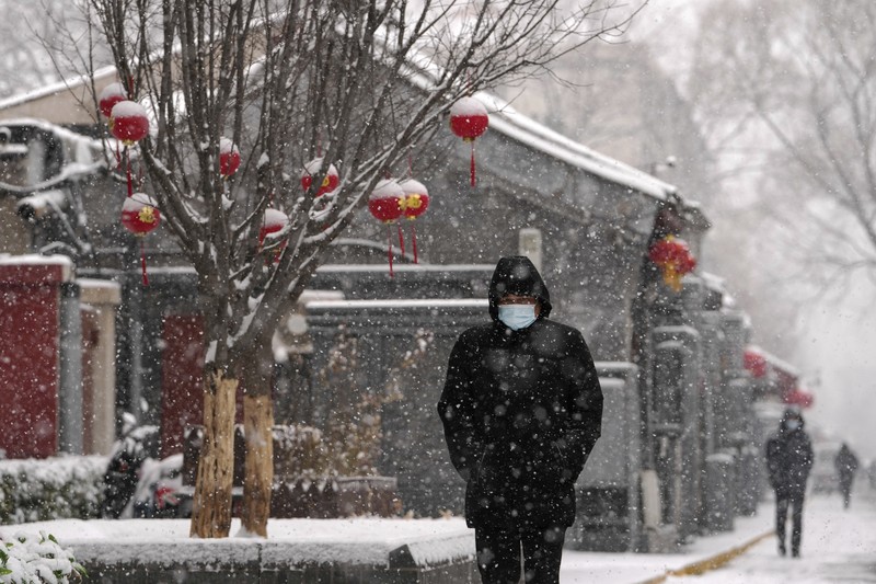 Seorang pria berlari saat salju turun di Beijing, Minggu (13/2/2022). (AP Photo/Mark Baker)