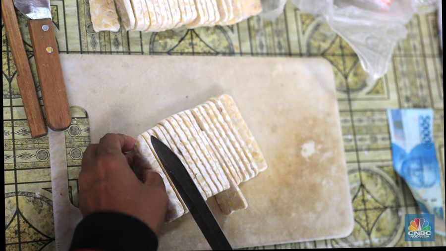 Pedagang tempe melayani pembeli di Pasar Kebayoran Lama, Jakarta, Selasa (15/2/2022). Lonjakan harga kedelai global berdampal bagi industri tempe dan tahu di dalam negeri, yang didominasi skala rumah tangga.(CNBC Indonesia/ Muhammad Sabki)