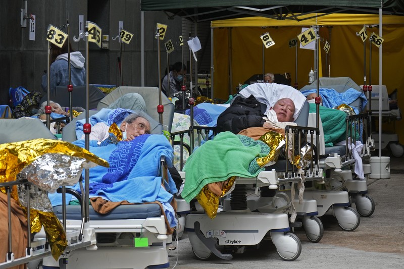 Patients lie on hospital beds as they wait at a temporary holding area outside Caritas Medical Centre in Hong Kong Wednesday, Feb.16, 2022. There was visible evidence that Hong Kong hospitals were becoming overwhelmed by the latest COVID surge, with patients on stretchers and in tents being seen to by medical personnel on Wednesday outside the Caritas hospital. (AP Photo Vincent Yu)