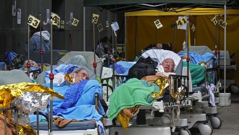 Patients lie on hospital beds as they wait at a temporary holding area outside Caritas Medical Centre in Hong Kong Wednesday, Feb.16, 2022. There was visible evidence that Hong Kong hospitals were becoming overwhelmed by the latest COVID surge, with patients on stretchers and in tents being seen to by medical personnel on Wednesday outside the Caritas hospital. (AP Photo Vincent Yu)