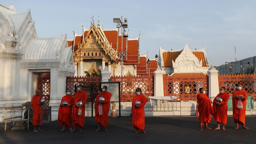 Buddhist monks wearing face masks to protect themselves from the coronavirus wait in line to receive alms during a morning alms offerings in front of Marble Temple in Bangkok, Thailand, Friday, April 16, 2021. (AP Photo/Sakchai Lalit)