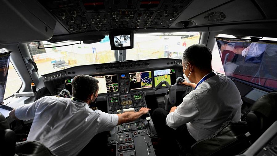 Seorang pilot dan seorang pengunjung duduk di kokpit Embraer E190-E2 di Singapore Airshow di Singapura, Rabu (16/2/2022). (REUTERS/Caroline Chia)