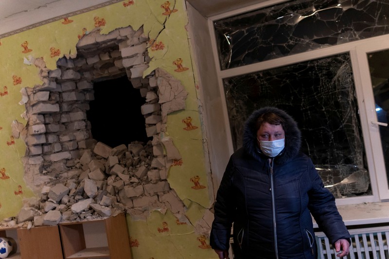 Seorang penduduk setempat berdiri di dekat sebuah lubang di dinding di dalam ruang kelas taman kanak-kanak, yang menurut pejabat militer Ukraina, dirusak oleh penembakan, di Stanytsia Luhanska di wilayah Luhansk, Ukraina, Kamis (17/2/2022). (REUTERS/Carlos Barria)