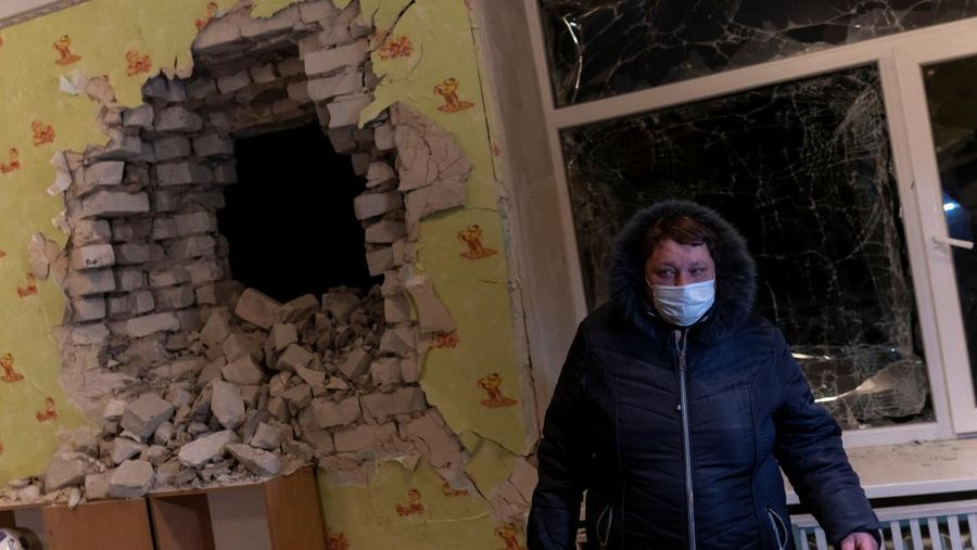 Seorang penduduk setempat berdiri di dekat sebuah lubang di dinding di dalam ruang kelas taman kanak-kanak, yang menurut pejabat militer Ukraina, dirusak oleh penembakan, di Stanytsia Luhanska di wilayah Luhansk, Ukraina, Kamis (17/2/2022). (REUTERS/Carlos Barria)