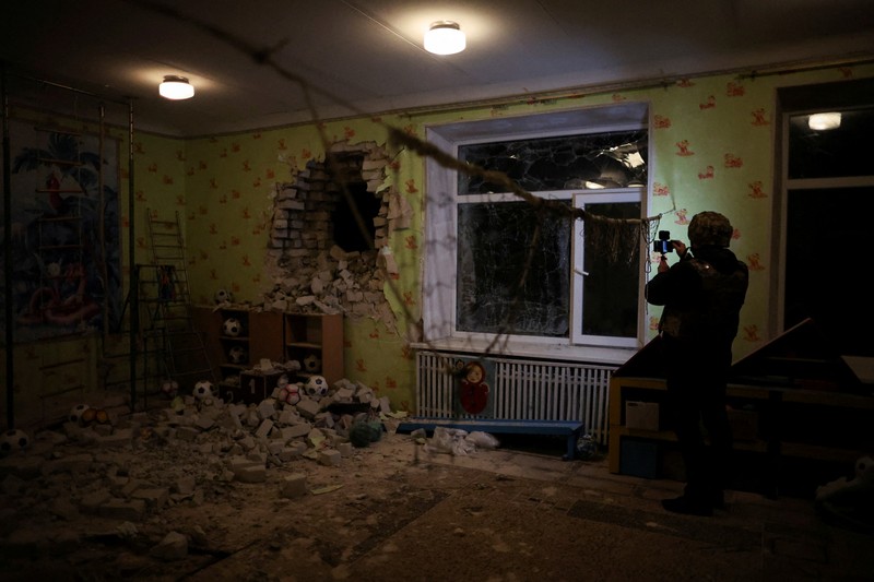 Seorang penduduk setempat berdiri di dekat sebuah lubang di dinding di dalam ruang kelas taman kanak-kanak, yang menurut pejabat militer Ukraina, dirusak oleh penembakan, di Stanytsia Luhanska di wilayah Luhansk, Ukraina, Kamis (17/2/2022). (REUTERS/Carlos Barria)