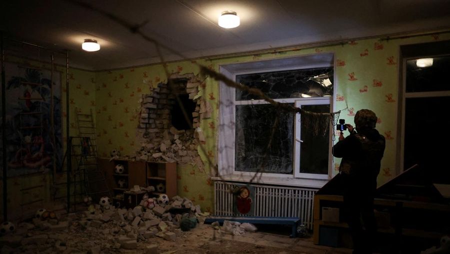 Seorang penduduk setempat berdiri di dekat sebuah lubang di dinding di dalam ruang kelas taman kanak-kanak, yang menurut pejabat militer Ukraina, dirusak oleh penembakan, di Stanytsia Luhanska di wilayah Luhansk, Ukraina, Kamis (17/2/2022). (REUTERS/Carlos Barria)