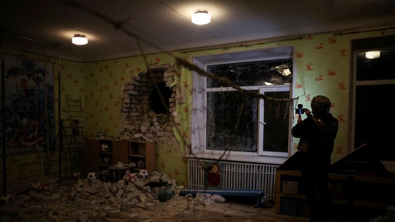 Seorang penduduk setempat berdiri di dekat sebuah lubang di dinding di dalam ruang kelas taman kanak-kanak, yang menurut pejabat militer Ukraina, dirusak oleh penembakan, di Stanytsia Luhanska di wilayah Luhansk, Ukraina, Kamis (17/2/2022). (REUTERS/Carlos Barria)