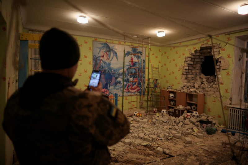 Seorang penduduk setempat berdiri di dekat sebuah lubang di dinding di dalam ruang kelas taman kanak-kanak, yang menurut pejabat militer Ukraina, dirusak oleh penembakan, di Stanytsia Luhanska di wilayah Luhansk, Ukraina, Kamis (17/2/2022). (REUTERS/Carlos Barria)