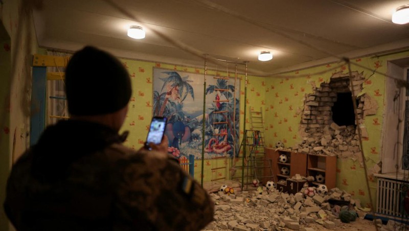 Seorang penduduk setempat berdiri di dekat sebuah lubang di dinding di dalam ruang kelas taman kanak-kanak, yang menurut pejabat militer Ukraina, dirusak oleh penembakan, di Stanytsia Luhanska di wilayah Luhansk, Ukraina, Kamis (17/2/2022). (REUTERS/Carlos Barria)