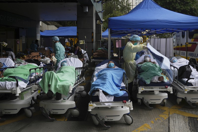Pasien berbaring di ranjang rumah sakit saat mereka menunggu di area perawatan sementara di luar Caritas Medical Center di Hong Kong, Jumat (18/2/2022). Rumah sakit Hong Kong mencapai kapasitas 90% pada hari Kamis dan fasilitas karantina sudah mencapai batasnya, kata pihak berwenang, ketika kota itu berjuang untuk memadamkan rekor jumlah kasus baru COVID-19. (AP Photo/Kin Cheung)