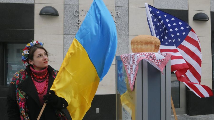 A woman holds a Ukraine flag and looks up at the traditional Ukrainian bread and salt in front of the US embassy in Kiev, Ukraine, Friday, Jan. 20, 2017, in support of Donald Trump hours before he is to be sworn in as president of the United States. (AP Photo/Efrem Lukatsky)