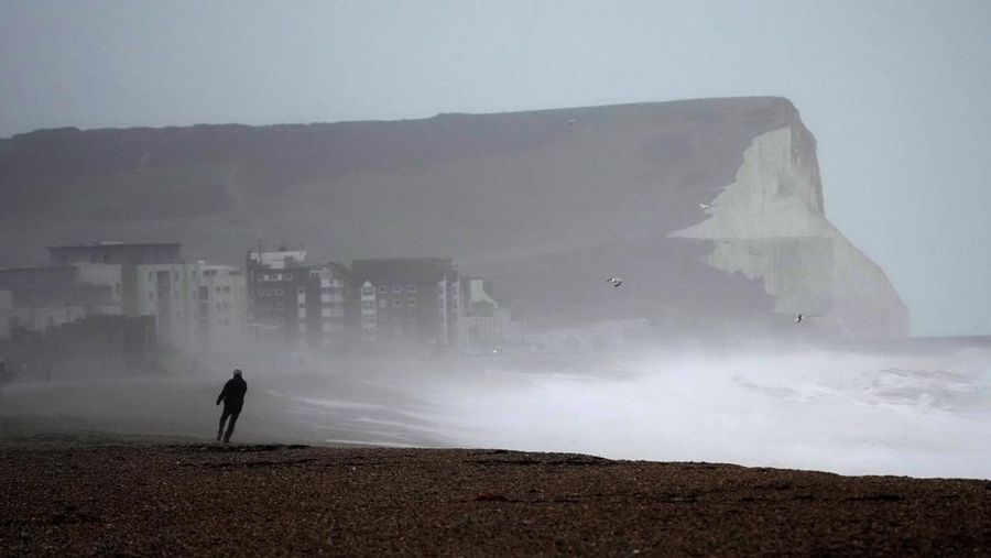 A person walks on Seaford Beach, as Storm Eunice hits Seaford and the south coast of England, Friday, Feb. 18, 2022. Millions of Britons are being urged to cancel travel plans and stay indoors Friday amid fears of high winds and flying debris as the second major storm this week prompted a rare 