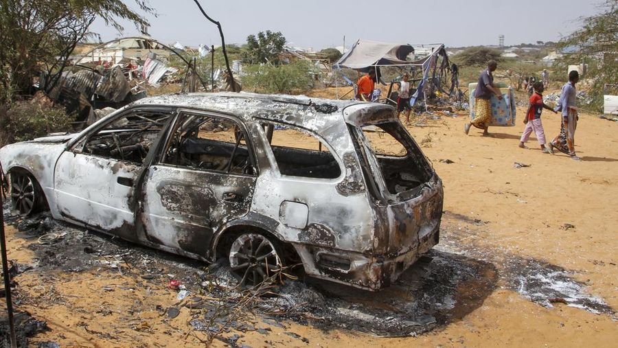 People walk past the wreckage of a vehicle destroyed in an attack on police and checkpoints on the outskirts of the capital Mogadishu, Somalia Wednesday, Feb. 16, 2022. The attack by the al-Shabab extremist group on Wednesday killed five people and wounded 16, police said. (AP Photo/Farah Abdi Warsameh)
